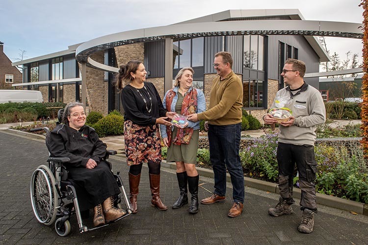 Wethouder Bouchtaoui reikt de prijs uit aan medewerkers van Hoveniersbedrijf de Plataan. 1 werknemer zit in een rolstoel. 